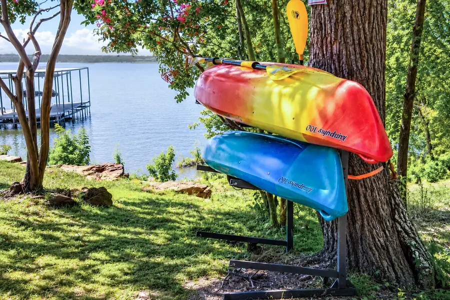 Two kayaks on a rack under a tree at the water's edge