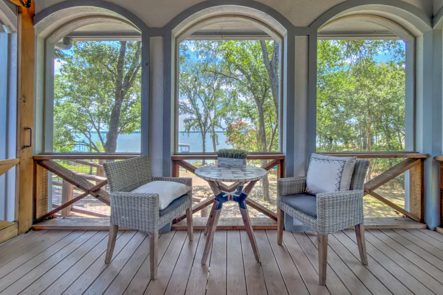 Two wicker chairs and a table on the screened porch, lake beyond the arches