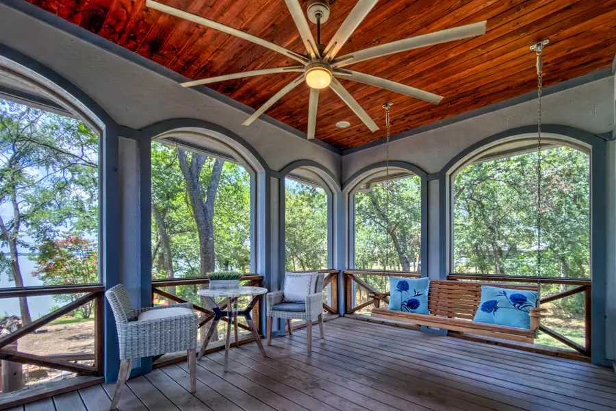 Screened porch with a wood ceiling, porch swing and views through the trees to the lake